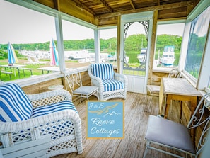 A covered porch with wicker furniture, a table, and a view of boats on a lake.