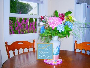 Ein Esstisch mit Blumen in einer Vase, zwei Holzstühle und ein Schild mit einem Vogel und Text.