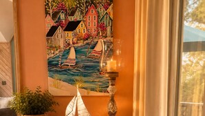 Een kamer met een houten bureau, een schilderij van huizen en een zeilboot, een kaars, en een klein model van een schip.