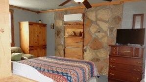 A bedroom with a bed, wooden dresser, stone wall, and a ceiling fan. - Rustic Charm Cabin for Families, Couples, or Fishing, Hunting  ON Norfork Lake!  (Gamaliel)