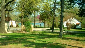 A rustic cabin with a stone foundation, surrounded by a grassy area and trees. - Rustic Charm Cabin for Families, Couples, or Fishing, Hunting  ON Norfork Lake!  (Gamaliel)