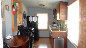 A compact kitchen with a dining table, a refrigerator, a stove, and a trash bin. - Rustic Charm Cabin for Families, Couples, or Fishing, Hunting  ON Norfork Lake!  (Gamaliel)