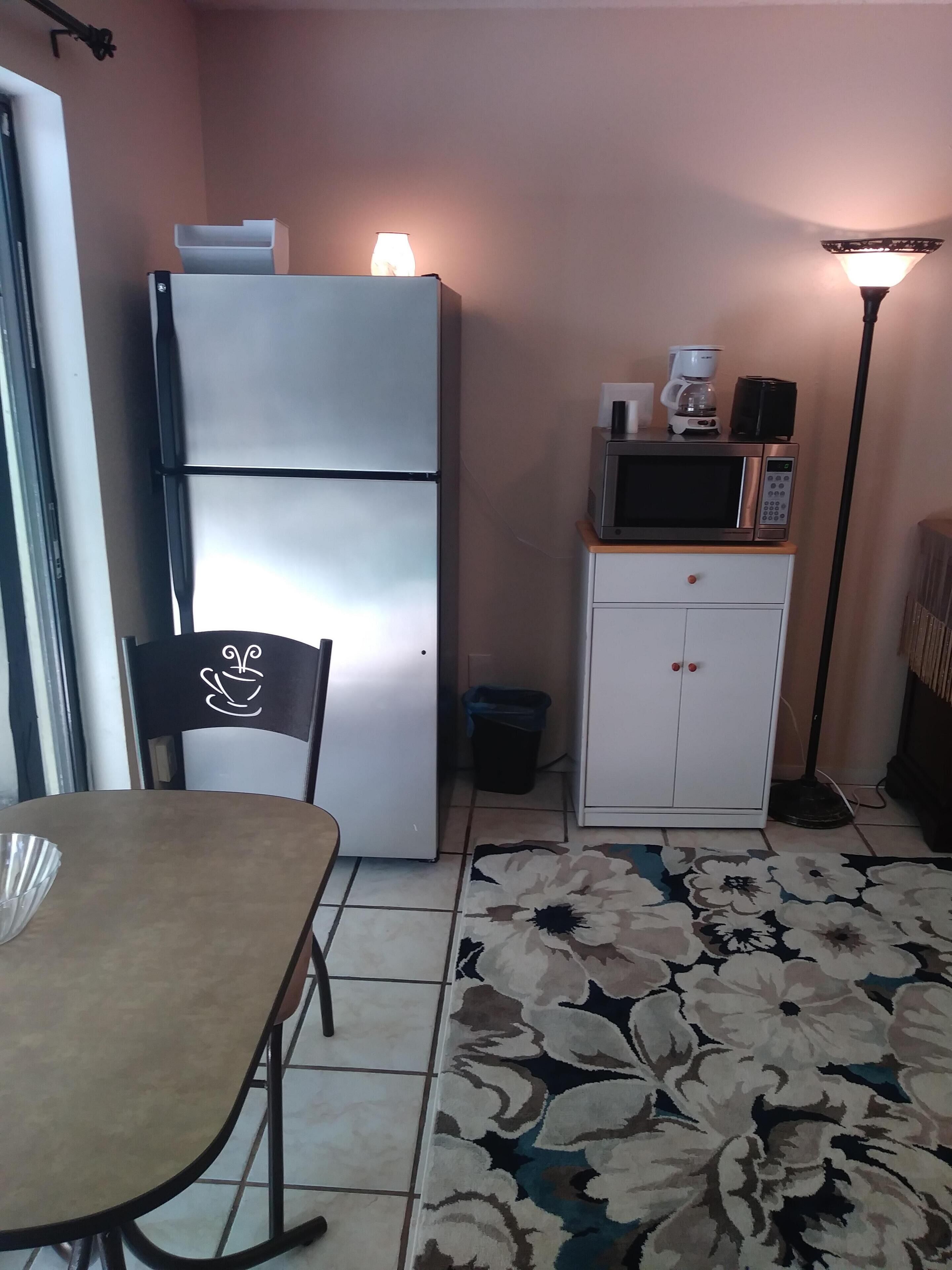 A compact kitchen with a refrigerator, microwave, and coffee maker on a small cabinet.