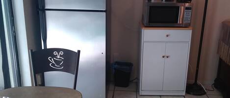 A compact kitchen with a refrigerator, microwave, and coffee maker on a small cabinet.