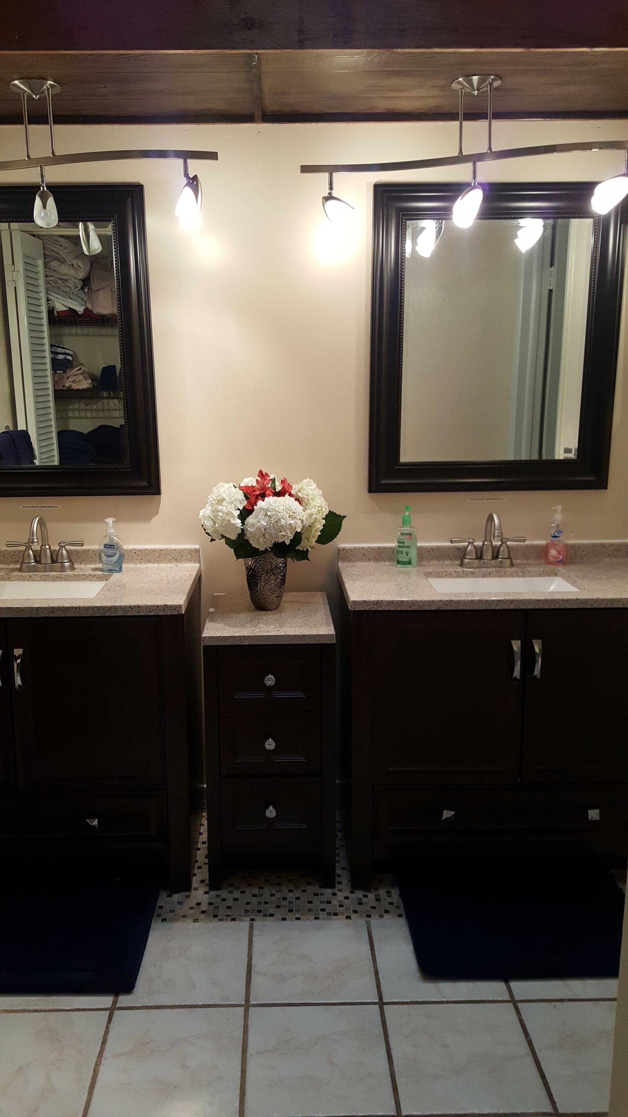 A bathroom with two sinks, a mirror, a vase with flowers, and a tiled floor.
