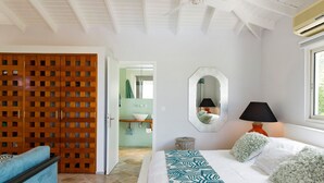 A bedroom with a bed, a wooden wardrobe, a mirror, and a window.