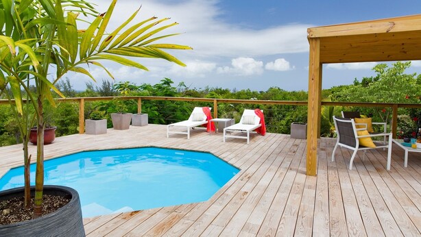 A wooden deck with a pool, white lounge chairs, and a pergola.