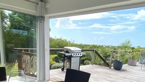 An outdoor patio with a round table and wicker chairs, a grill, and a view of the ocean.
