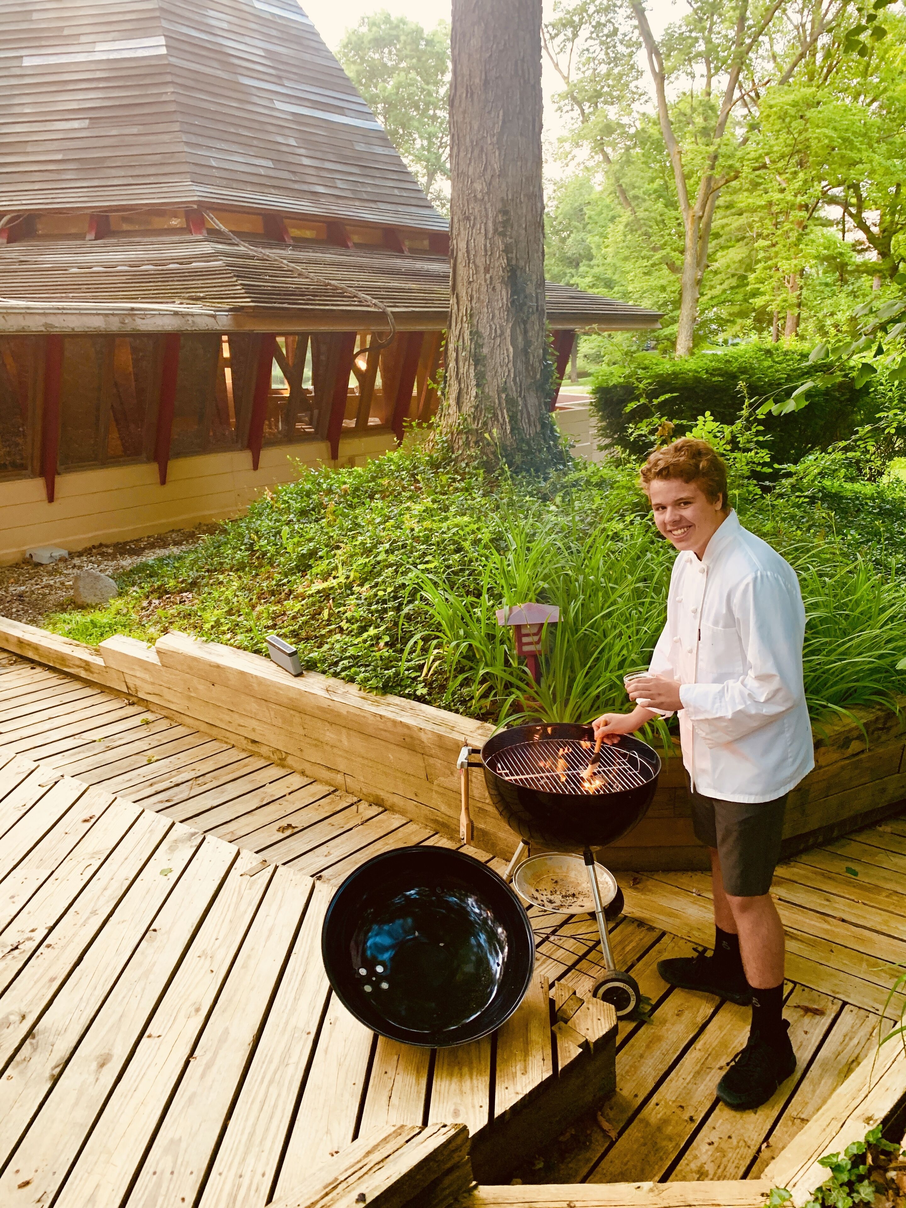 A person grilling outdoors with a wooden deck and a garden in the background.