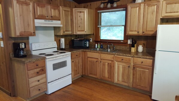 A kitchen with wooden cabinets, a white stove, a microwave, and a sink.