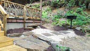 Un escalier en bois mène à une terrasse dotée d’une rambarde en treillis, le tout étant entouré de rochers et de pierres plates servant de marchepied.