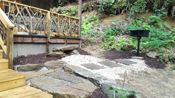 A wooden staircase leading to a deck with a lattice railing, surrounded by rocks and stepping stones.