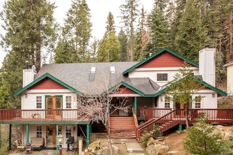 A two-story house with a porch, a staircase, and a view of the surrounding forest.