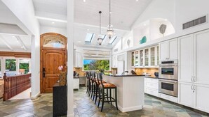 A spacious kitchen with a central island, white cabinetry, and a large wooden door. - Stunning Gated Home, Private Pool & Spa (Lahaina)