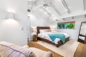 Une chambre avec un grand lit, un ventilateur de plafond, une fenêtre avec des stores et un miroir.