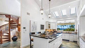 A spacious kitchen with a large island, white cabinetry, and a view of the ocean. - Stunning Gated Home, Private Pool & Spa (Lahaina)