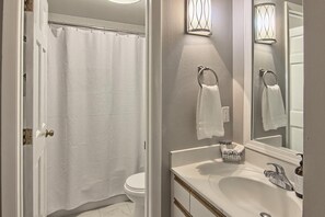 A bathroom with a white shower curtain, a toilet, a sink with a mirror, and a towel rack.
