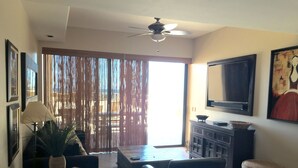 A living room with a sofa, armchair, coffee table, TV, and a ceiling fan. - In The Middle Of All, Ocean Front Ground Floor 2BD. Steps from the beach Phase 1 (Puerto penasco)