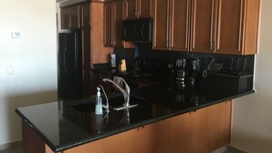 A modern kitchen with wooden cabinets, a black countertop, and stainless steel appliances. - In The Middle Of All, Ocean Front Ground Floor 2BD. Steps from the beach Phase 1 (Puerto penasco)
