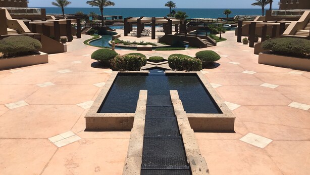 A resort pool area with a central water feature, surrounded by palm trees and a view of the ocean. - In The Middle Of All, Ocean Front Ground Floor 2BD. Steps from the beach Phase 1 (Puerto penasco)