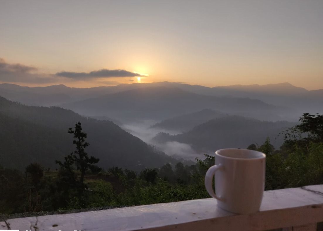 A mug on a wooden ledge overlooking a mountainous landscape during sunrise.