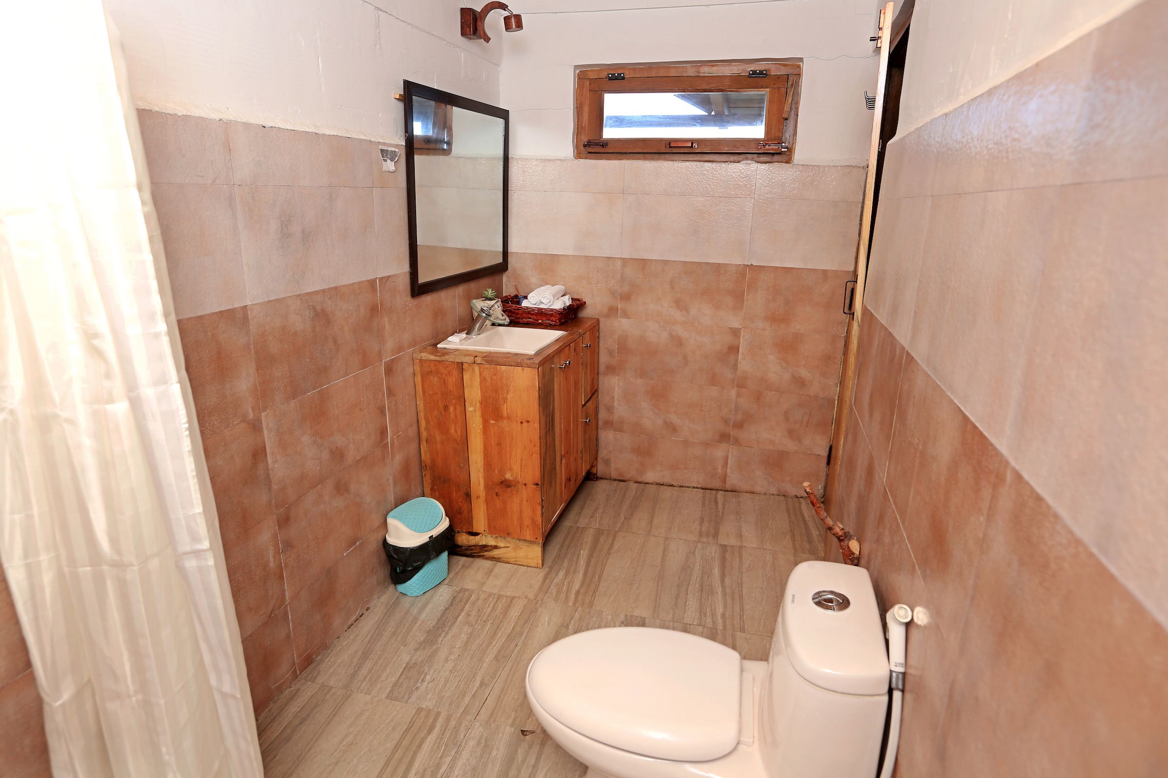 A small bathroom with a wooden cabinet, a toilet, and a window.