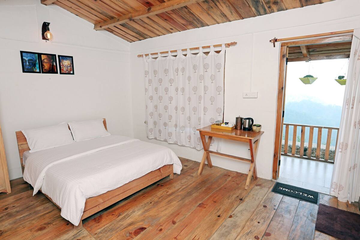 A bedroom with a wooden bed, a small wooden desk, a curtain with a tree pattern, and a balcony door.