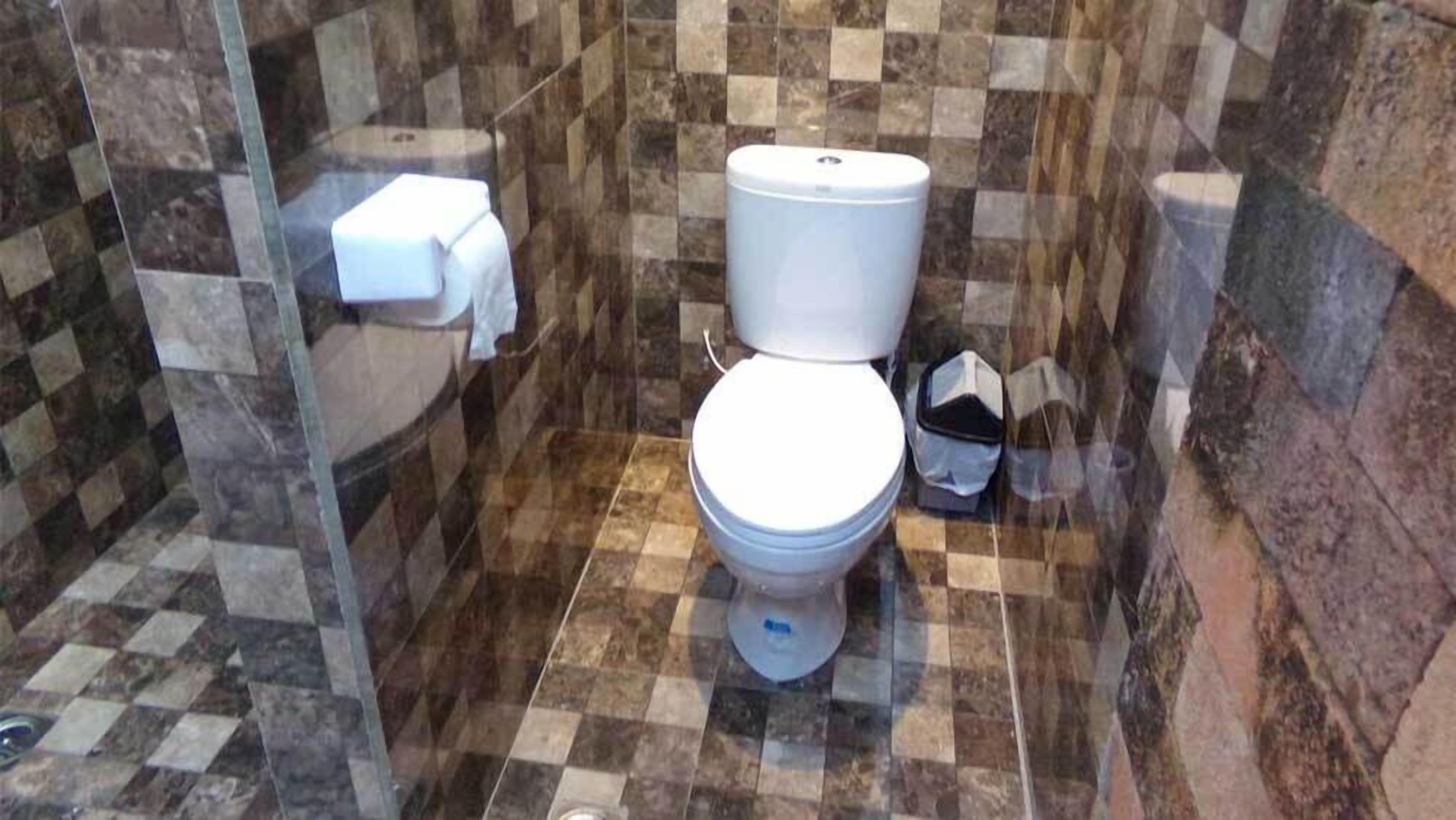 A bathroom with a toilet, a paper towel dispenser, and a shower area.