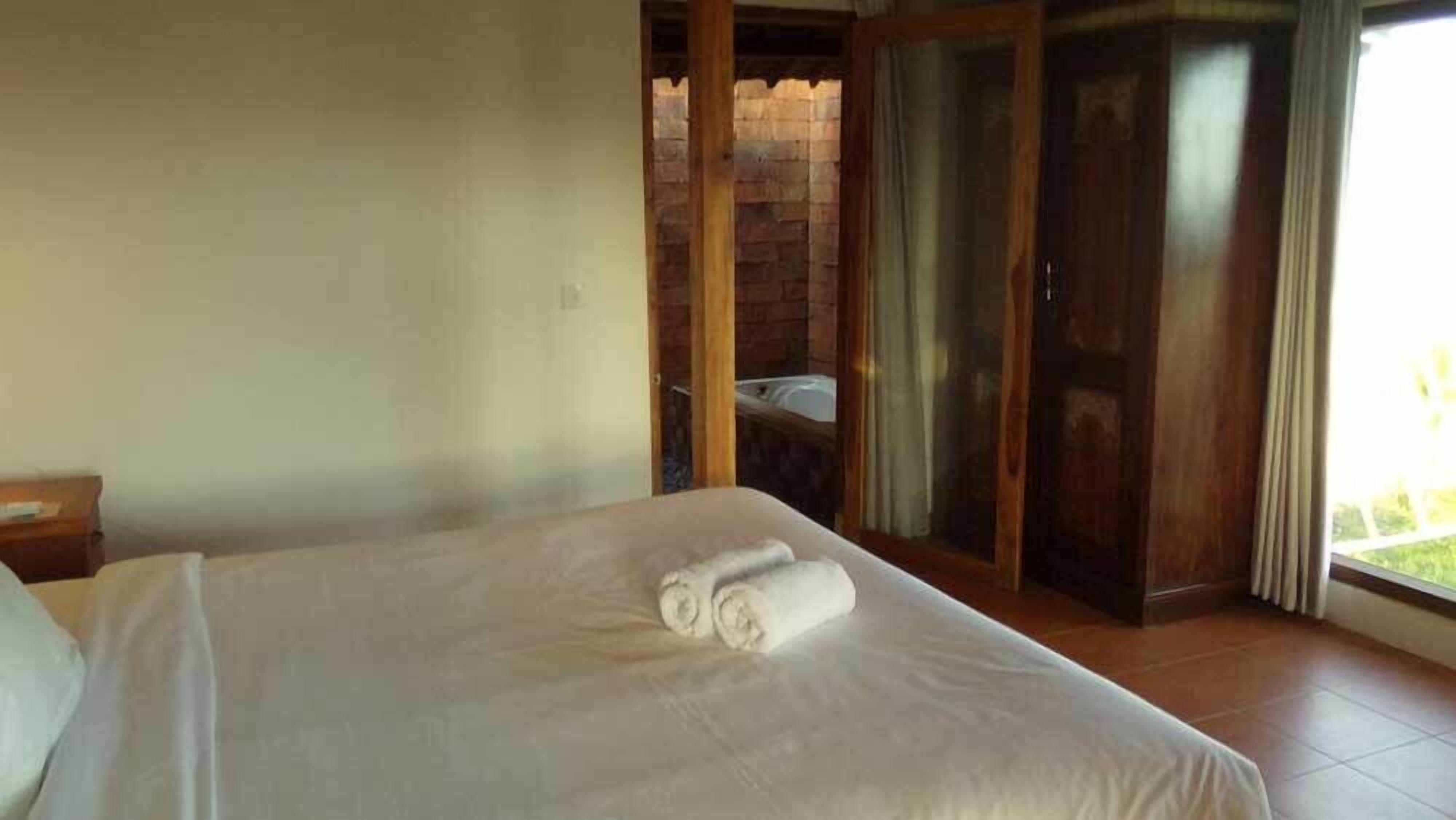 A hotel room with a bed, a nightstand, a bathroom with a shower, and a sliding glass door leading to an outdoor area.
