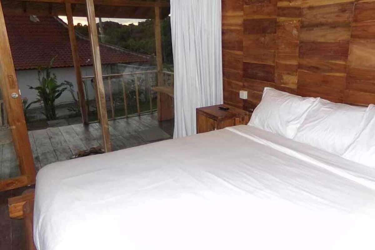 Un dormitorio con una cama grande, cabecera de madera y vista a un edificio de techos rojos a través de una puerta de cristal.