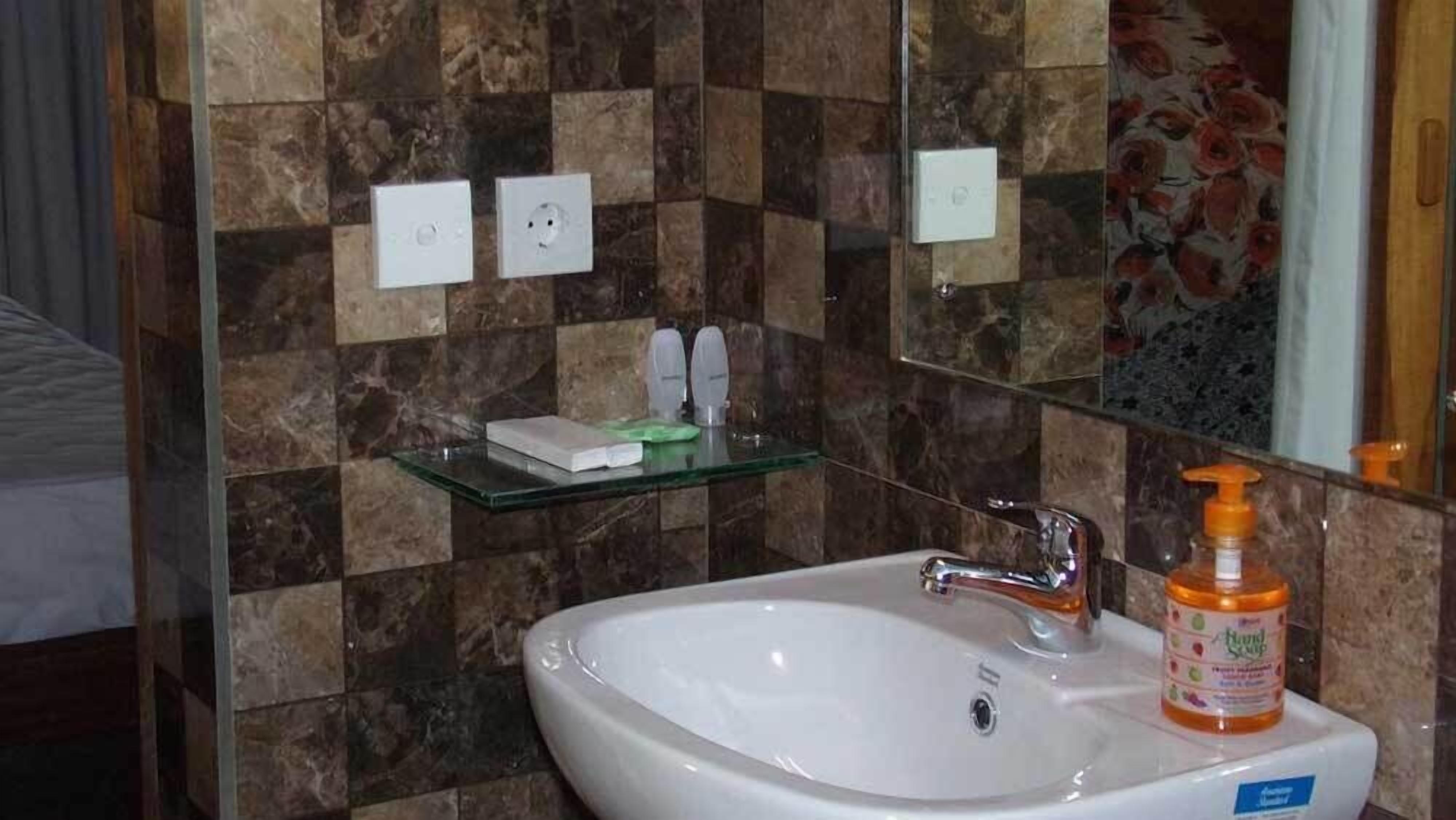 A bathroom with a white sink, a mirror, and a glass shelf with toiletries.