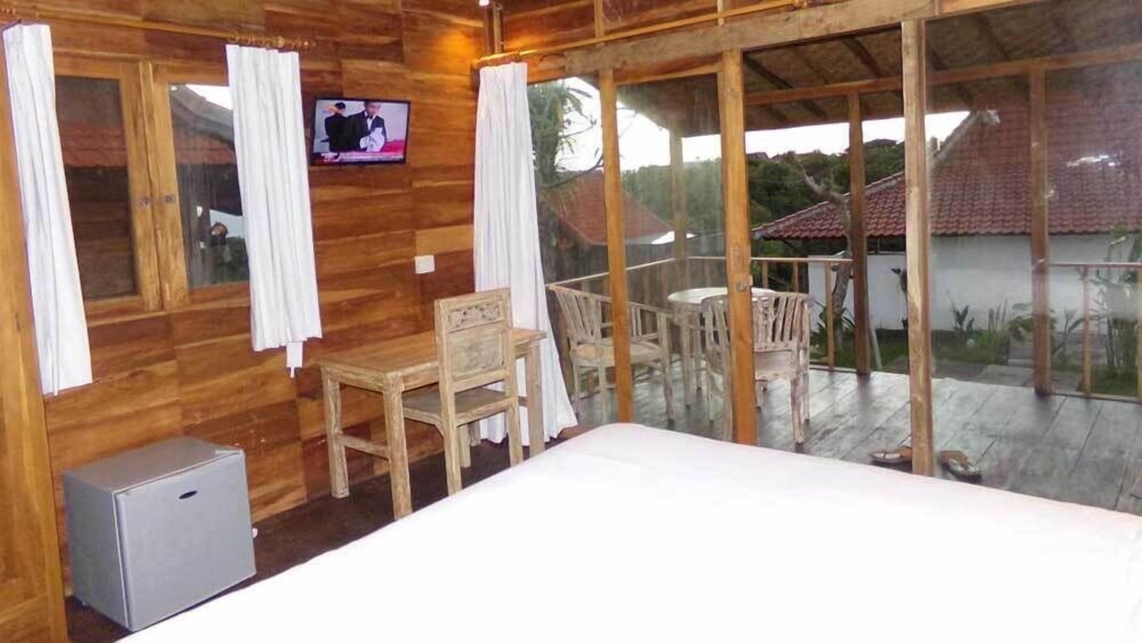 A wooden room with a bed, a small table, and chairs. There is a television on the wall and a balcony with a table and chairs.