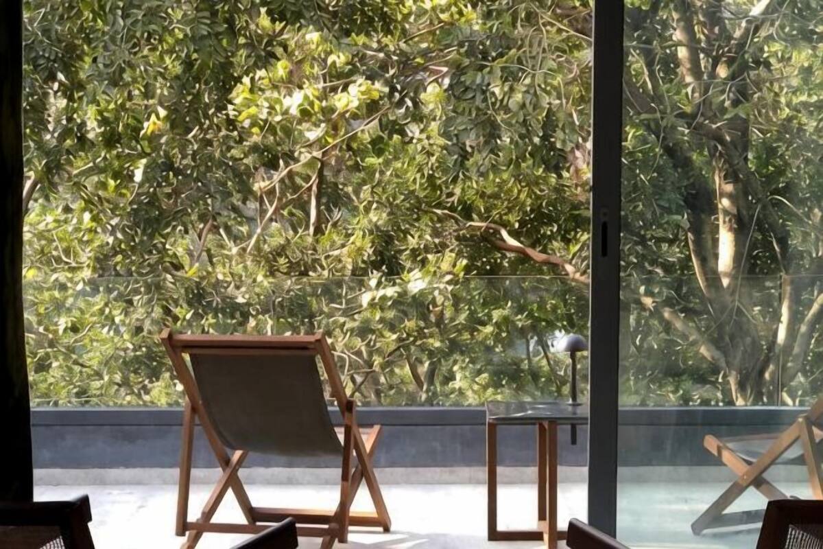 A room with a large window, a wooden chair, a small table, and a view of trees.