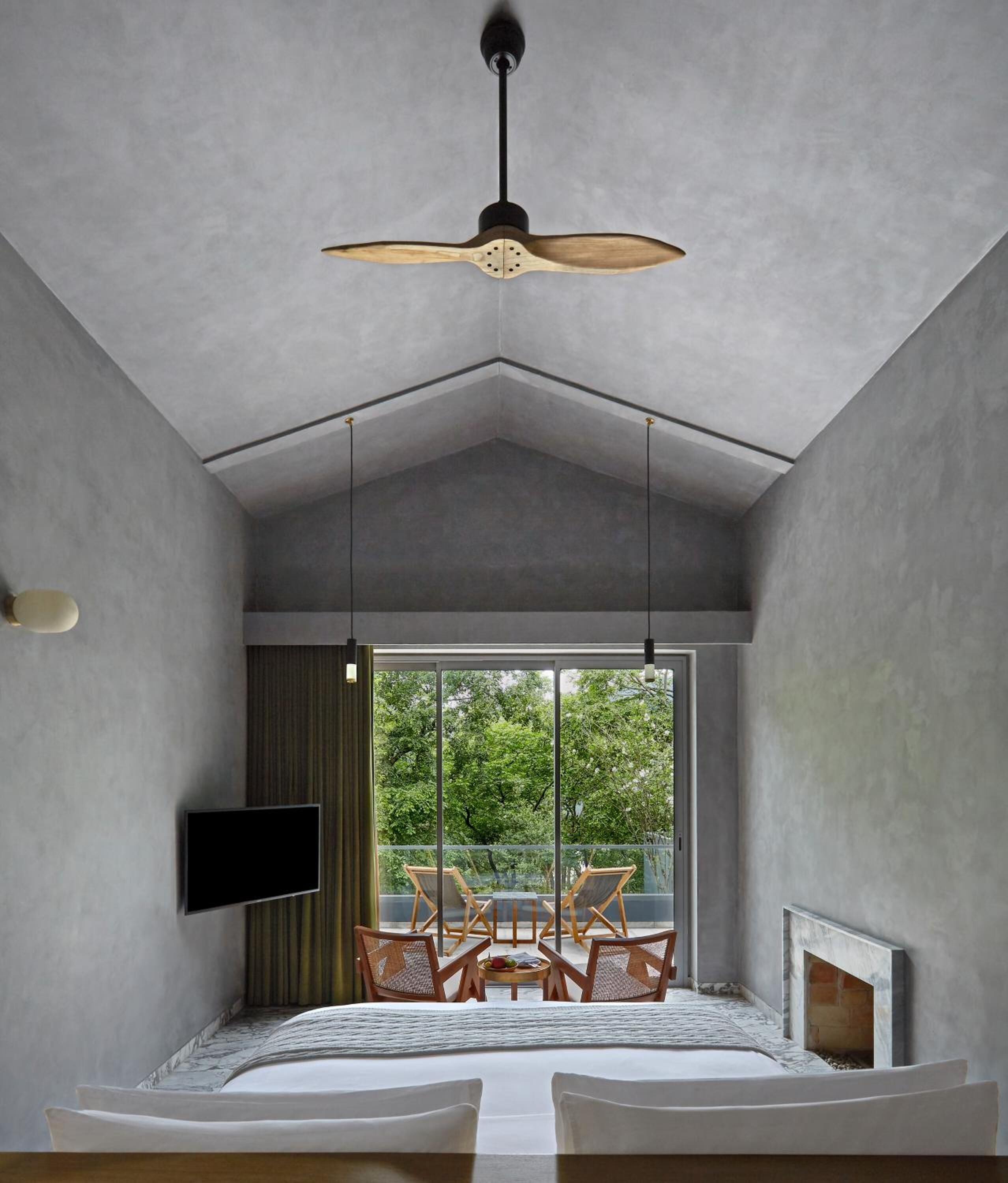 A modern bedroom with a large window, a ceiling fan, a flat-screen TV, and a fireplace.