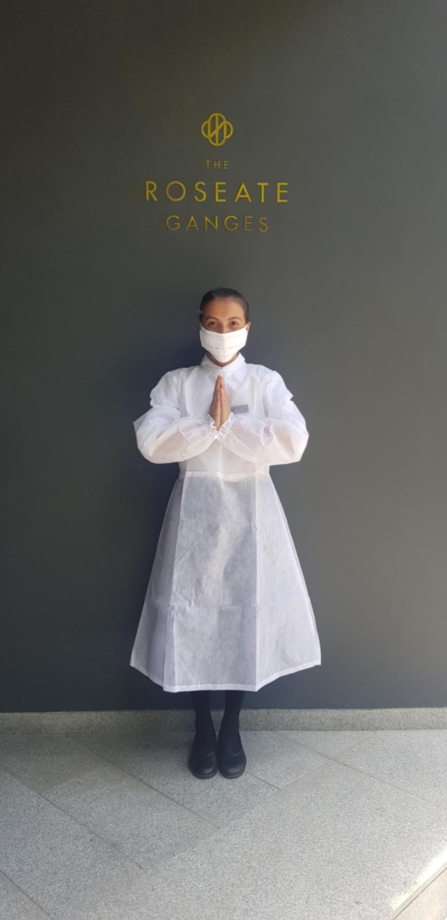 A person in a white dress standing against a dark wall with the text "THE ROSEATE GANGES" above them.