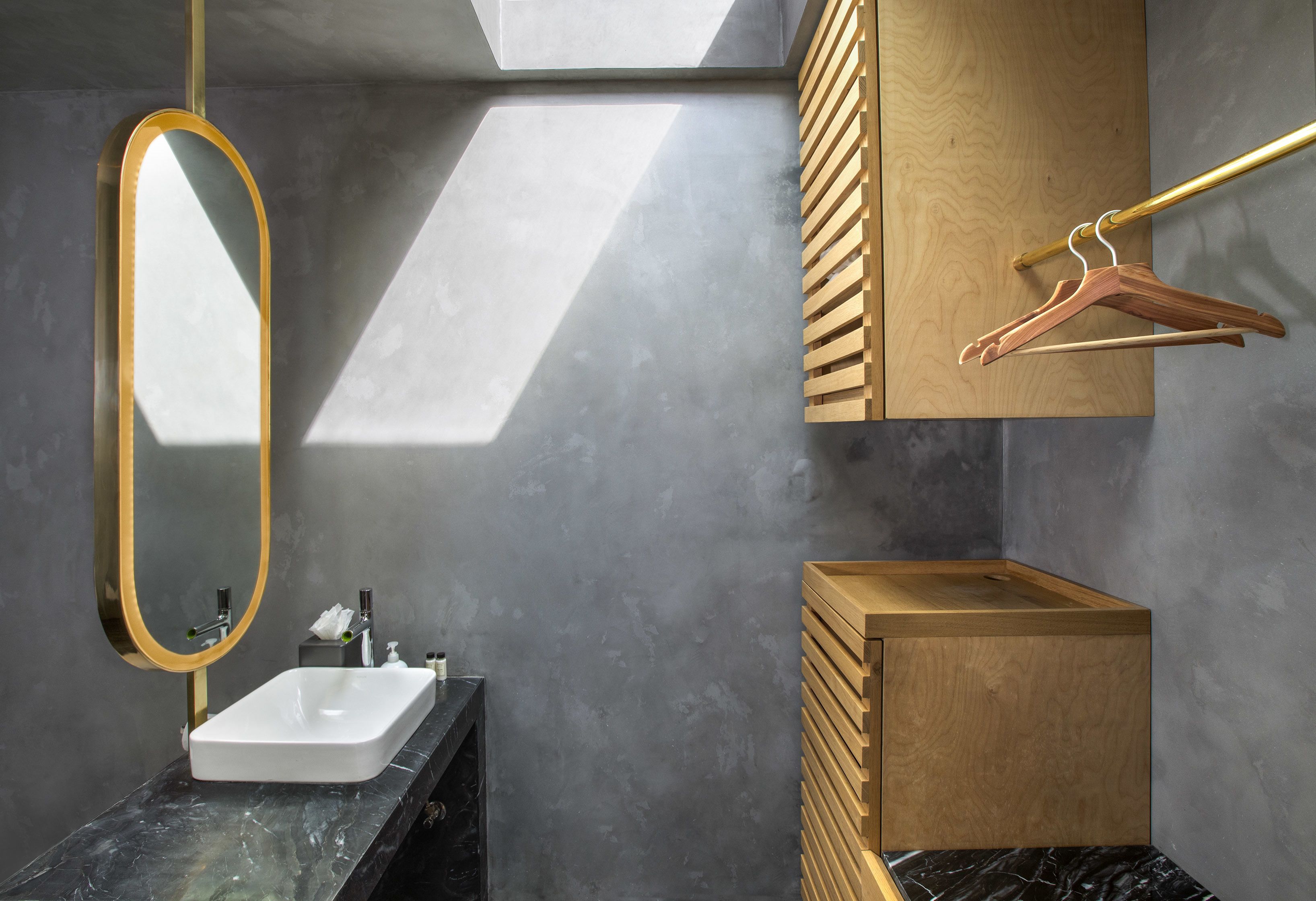 A modern bathroom with a rectangular sink, a gold-framed mirror, and a wooden vanity with a towel rack.