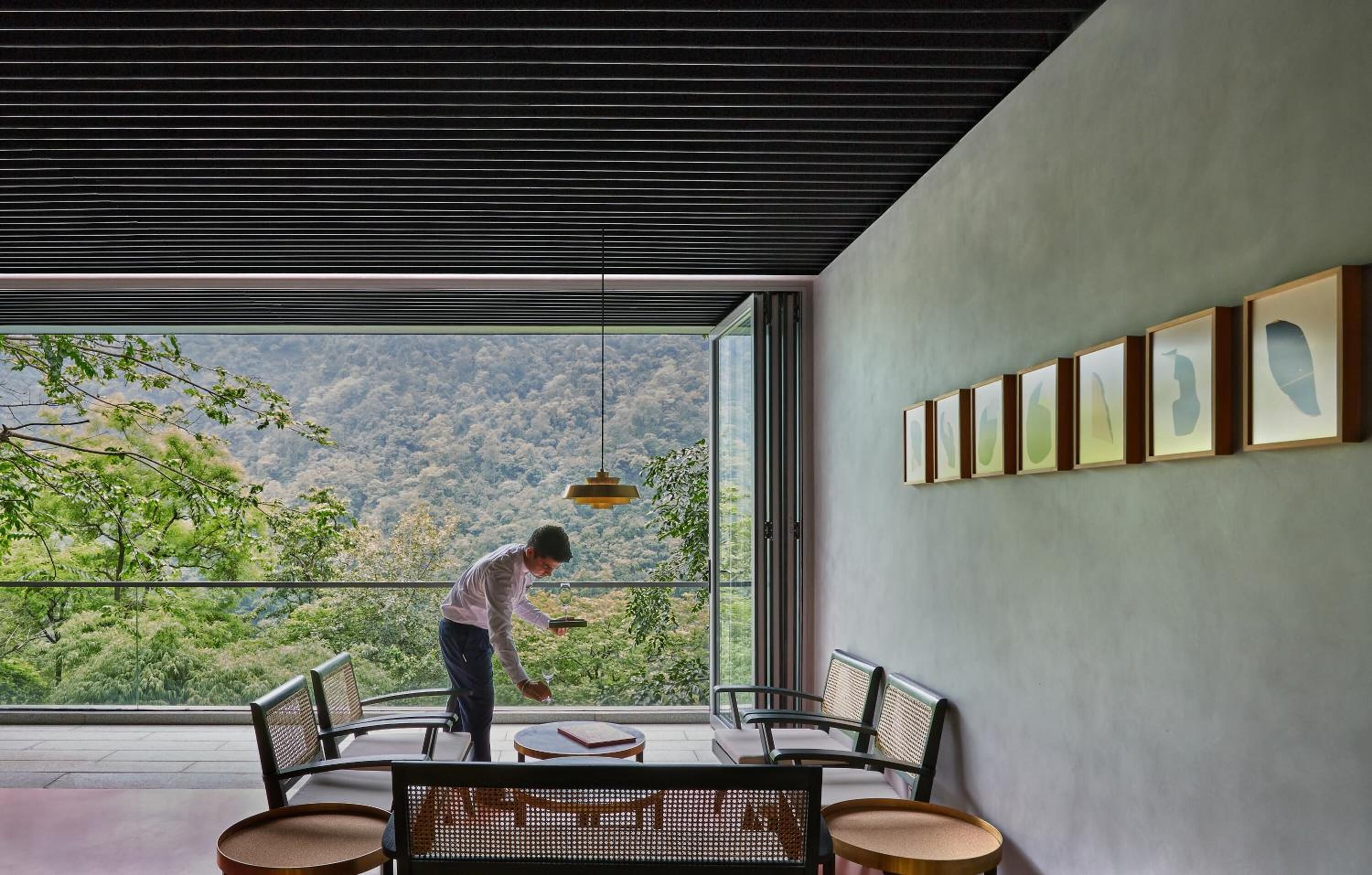 Une chambre moderne dotée d’une grande fenêtre, d’un coin repas avec des chaises et une table, et d’un mur orné de tableaux encadrés.