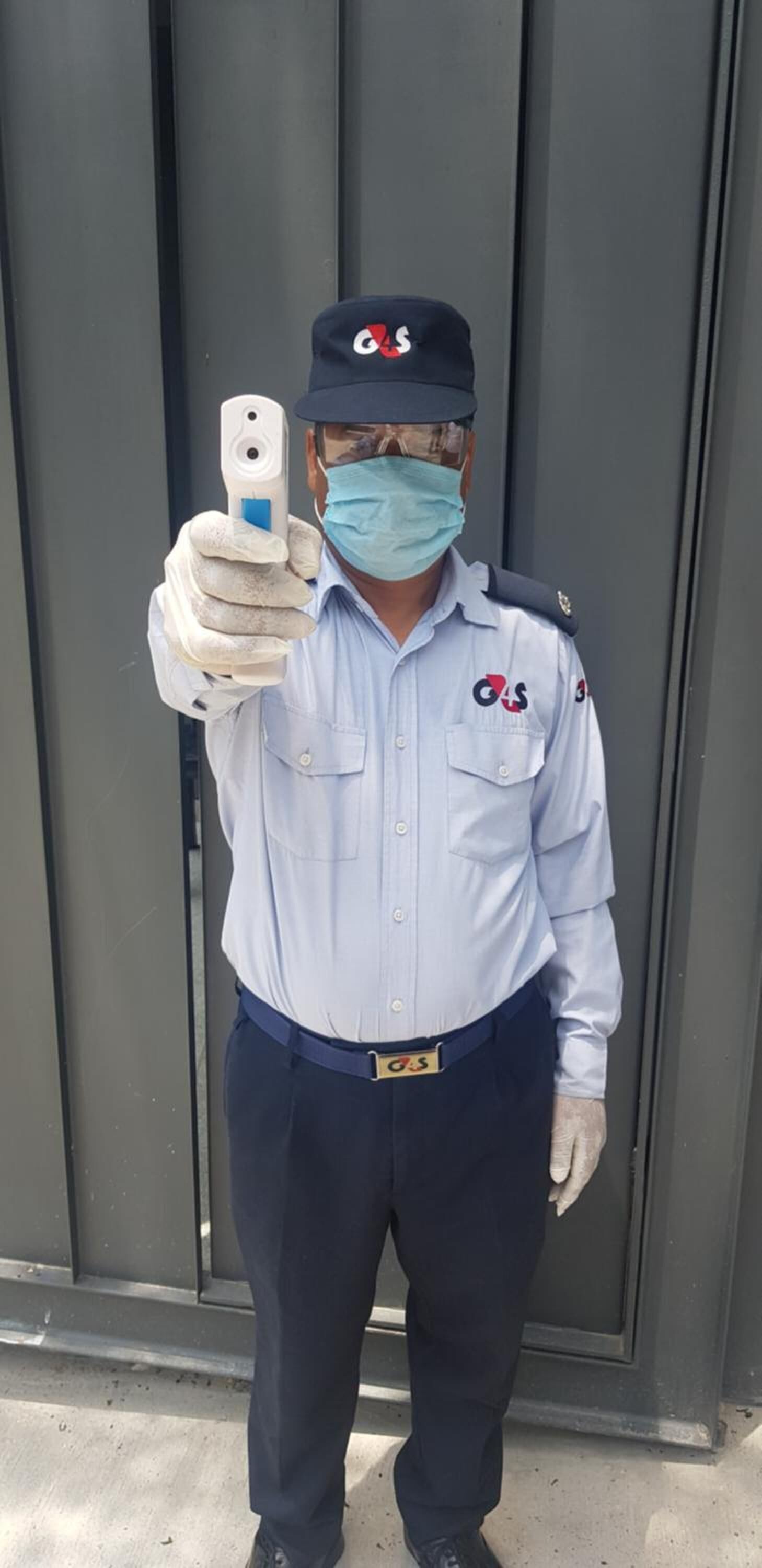 A uniformed individual in a light blue shirt and dark trousers, holding a smartphone.