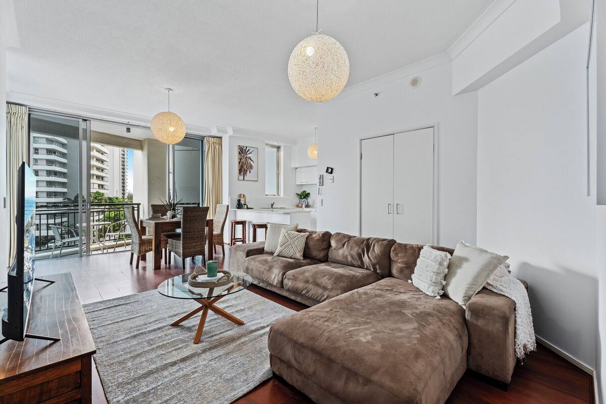 A modern living room with a brown sectional sofa, a glass coffee table, and a dining area with chairs and a table.