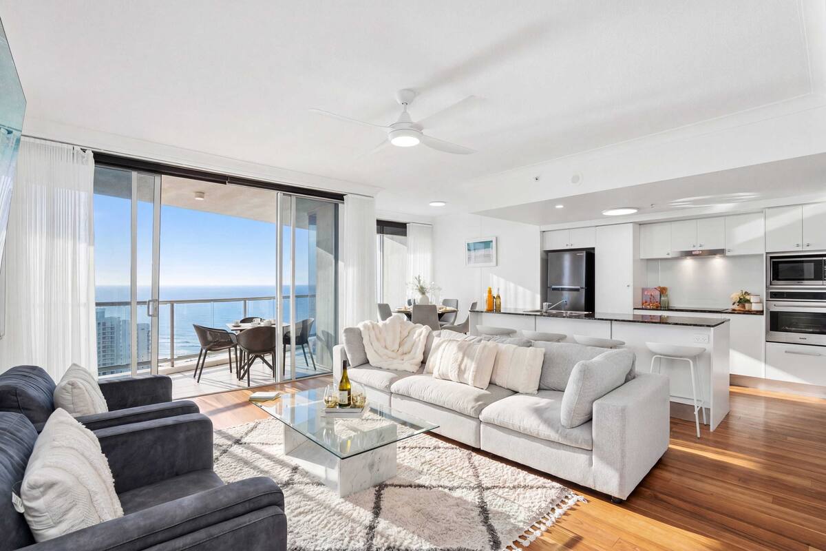 A modern living room with a sofa, a glass coffee table, and a dining area with chairs.