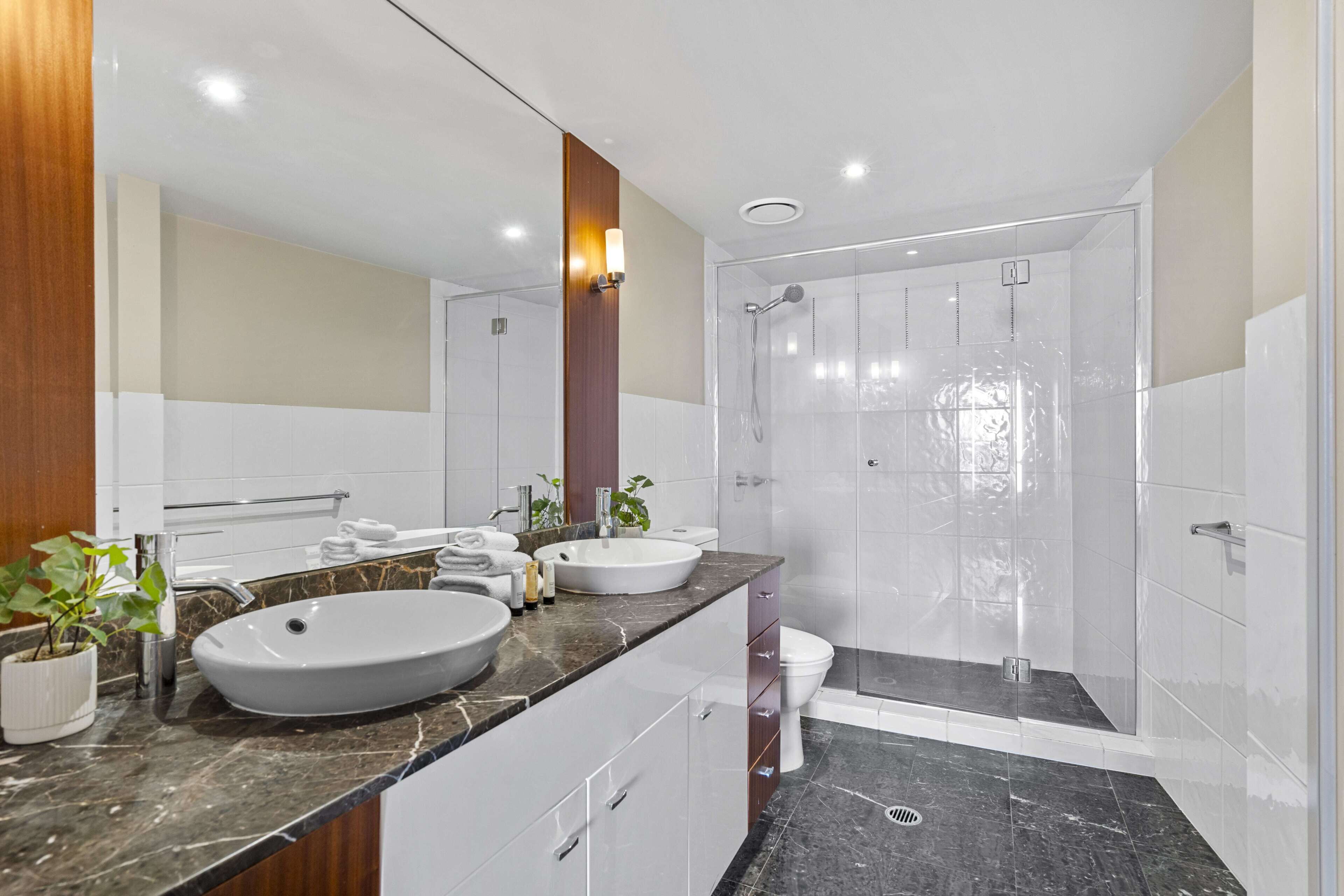 Un baño moderno con dos lavamanos, una ducha y un inodoro.