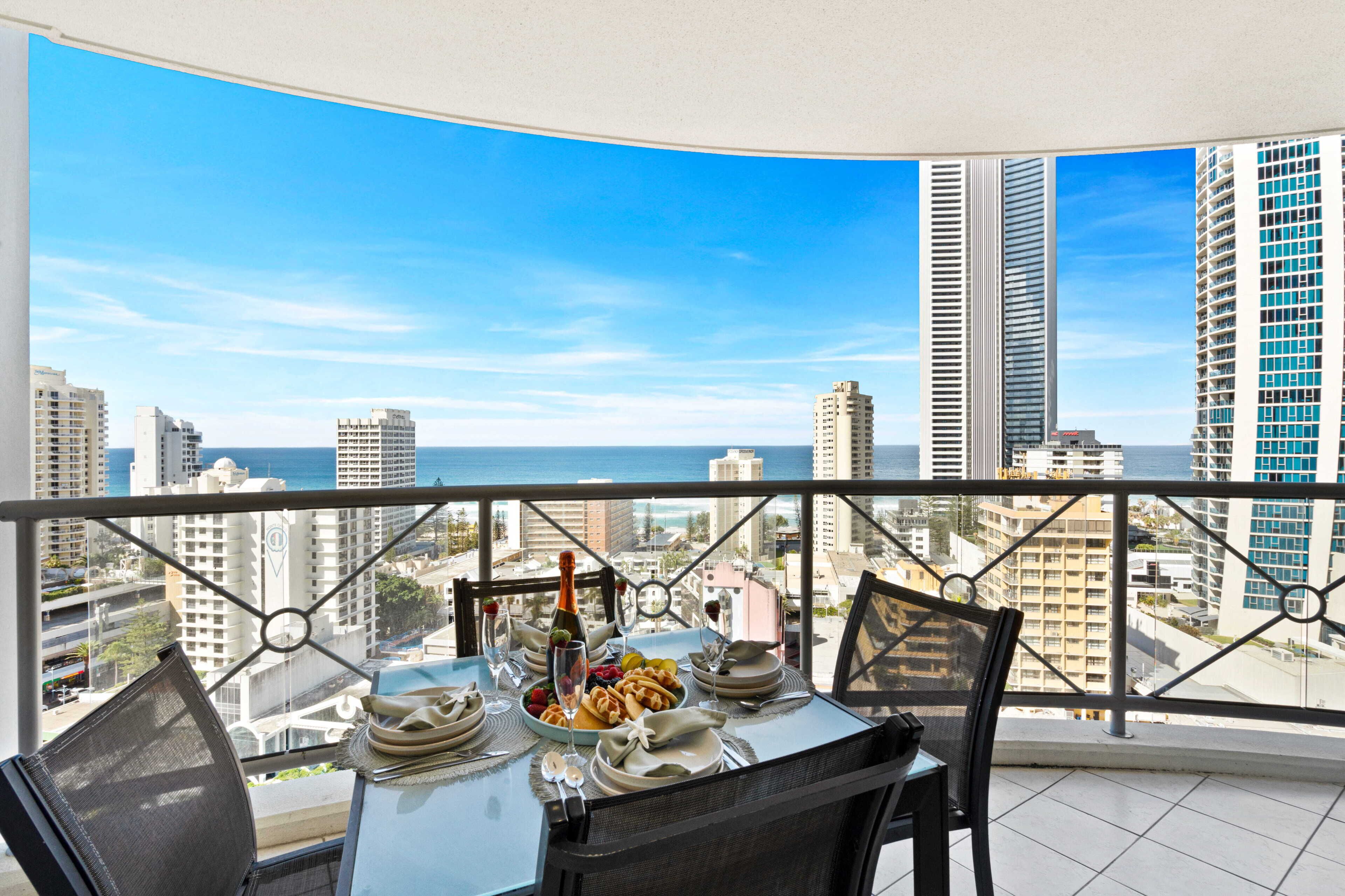 Un balcón con una mesa lista para comer, con vistas a un paisaje urbano de edificios altos y cielo despejado.