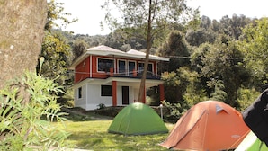 Une maison à deux étages, à la façade rouge et blanche, entourée d’une pelouse où sont installées deux tentes.