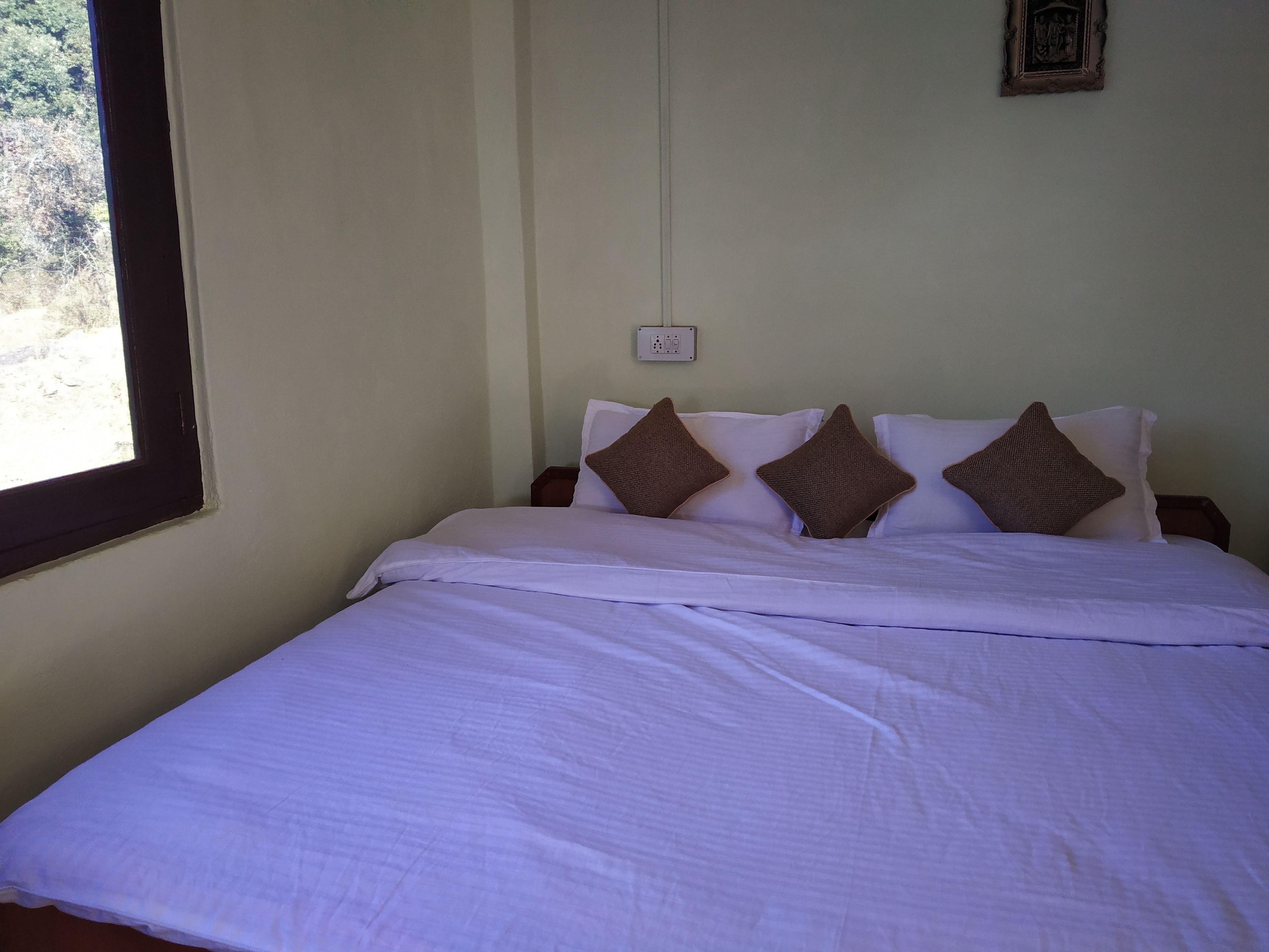 Una cama bien tendida con sábanas blancas y tres almohadas marrones.