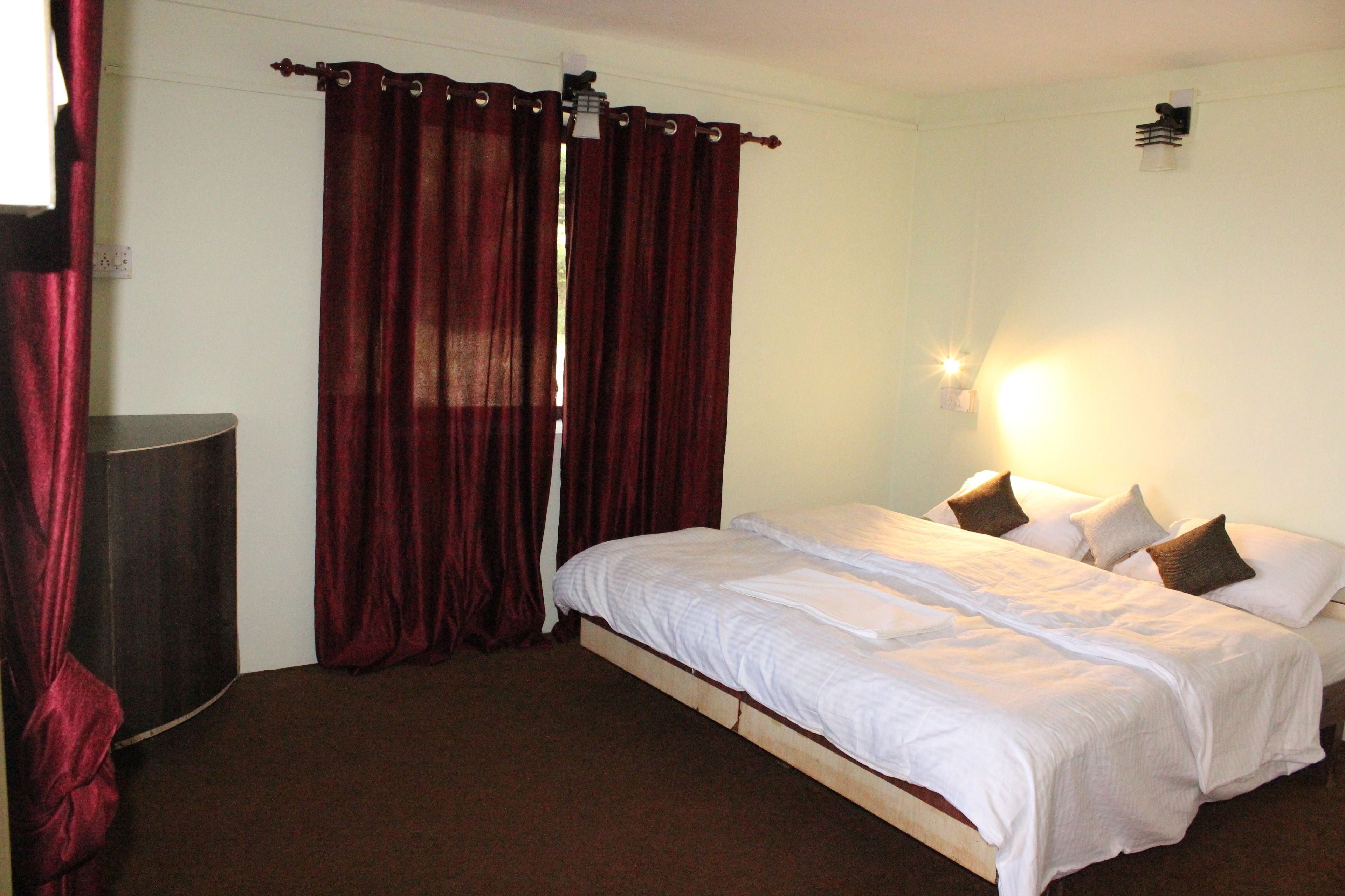 A bedroom with a bed, curtains, a bedside lamp, and a wall-mounted light fixture.