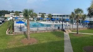 A pool area with lounge chairs and umbrellas, surrounded by a fence and palm trees. - Bogue Shores, King bed. Pool side, Beach and Sound Access-sleeps 4 (Atlantic Beach)