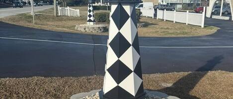 A lighthouse with a black and white diamond pattern, surrounded by a stone base and a white picket fence.