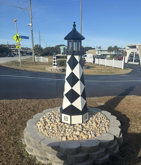 A lighthouse with a black and white diamond pattern, surrounded by a stone base and a white picket fence.