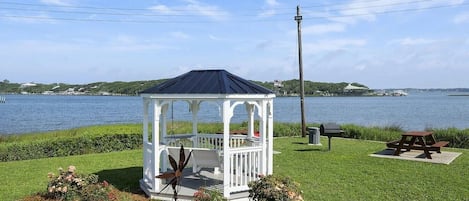 A gazebo with a white railing and a dark roof, surrounded by a well-maintained lawn and a picnic table.