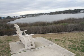 A concrete bench by a lake with a view of houses and boats in the distance.